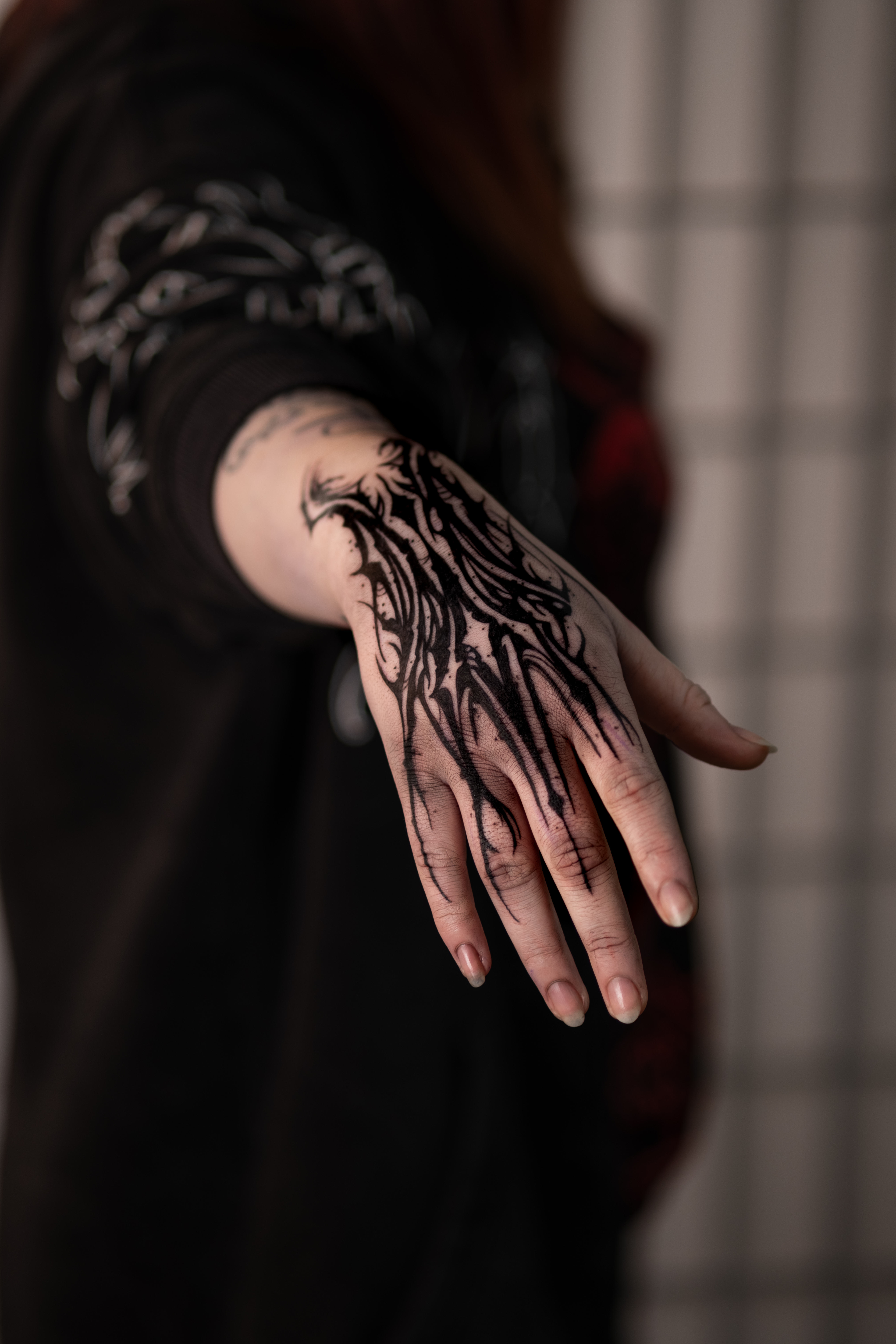 Person mit neutralem Blick streckt Hand mit schwarzem Tattoo aus